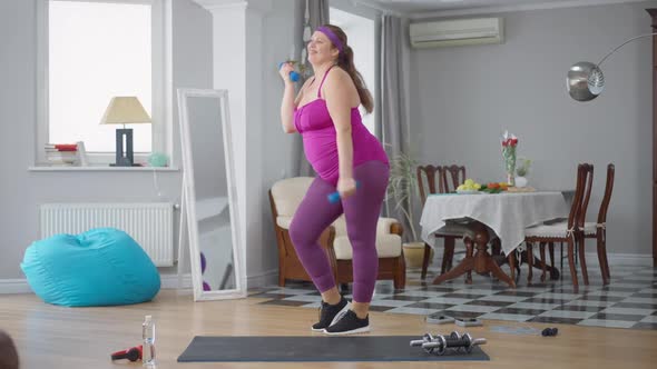 Wide Shot of Cheerful Motivated Overweight Woman Having Fun Working Out with Dumbbells at Home