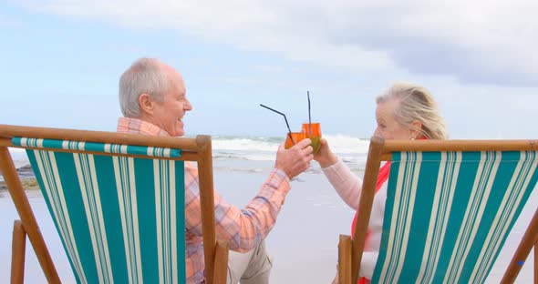 Side view of old caucasian senior couple toasting glasses of cocktail at beach 4k