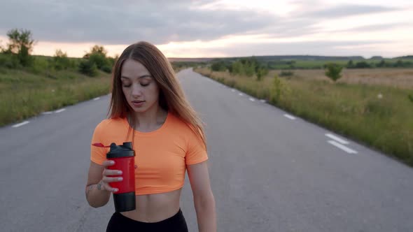 Young Athletic Girl Walking Drinking From Sport Flask and Looking at Camera