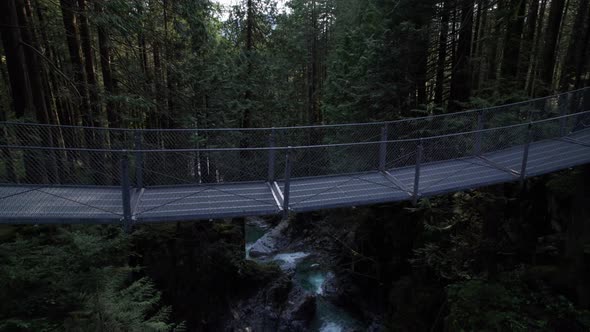 Flying over suspension bridge to reveal rushing forest mountain stream.