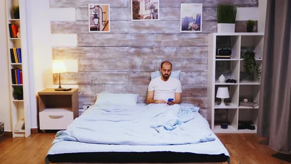 Caucasian Man in Bed Reading on His Phone