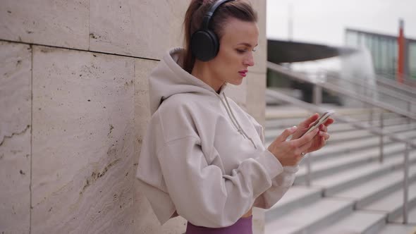 Sportswoman is Using Modern Mobile Phone and Wireless Headphones