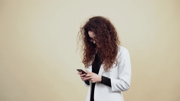 Happy Young Woman with Curly Hair Holds a Phone in Her Hand and Vb with Friends Through the Message