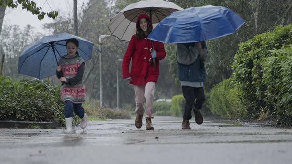 Three kids running happy in the rain and puddles with umbrellas