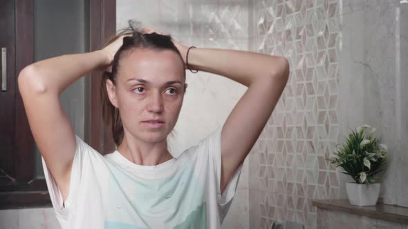 Young Brownhaired Woman Plaits Long Silky Hair in Front of Mirror in Ponytail