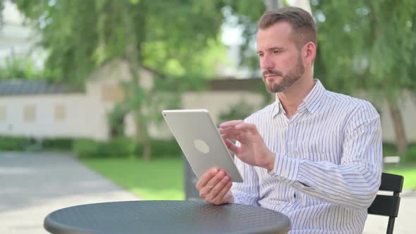 Attractive Middle Aged Man Using Tablet in Outdoor Cafe