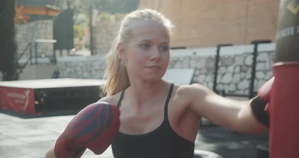 Woman Punching Bag In Boxing Gloves At Outdoor Gym