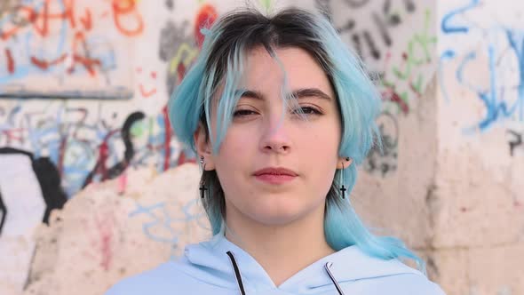 Blue haired teenage girl in light blue hoodie against graffiti wall. Head portrait