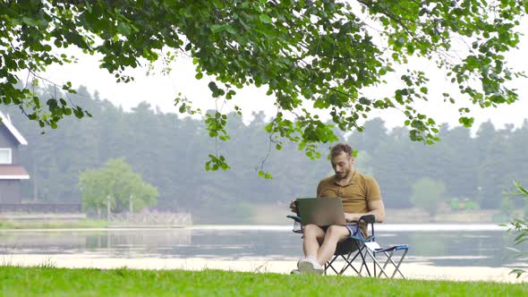 Man working with computer by lake in nature.