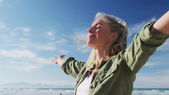 Caucasian woman with arms wide, smiling at the beach on sunny day