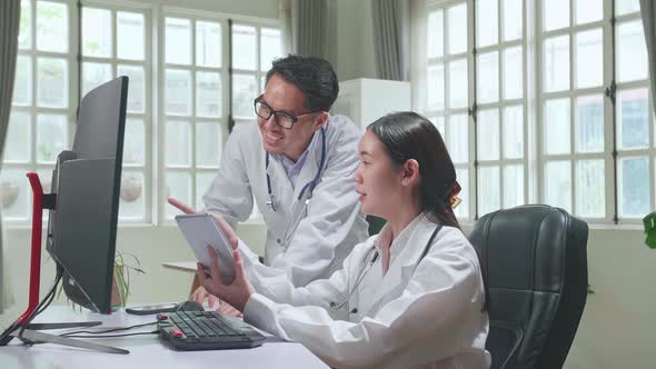 Medical Office: Two Asian Professional Physicians Talking, Consulting And Working On Tablet