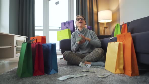 Happy Woman Is Sitting on a Carpet in a Cozy Room Among Shopping Bags and Making Money Rain From US