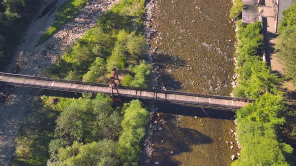 Aerial View From Old Wooden Suspension Bridge Over a Mountain River. Girl Standing on a Wooden