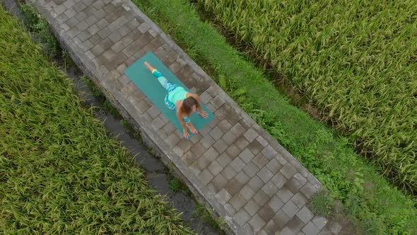 Aerial Slowmotion Shot of a Young Woman Practicing Yoga on a Beautiful Rice Field