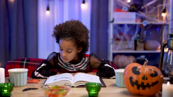 Little African American Girl in Festive Costume Reads Book with Enthusiasm