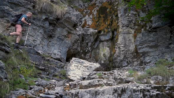 Man Hiker with a Backpack and Trekking Poles is Walking in the Rocky Mountains