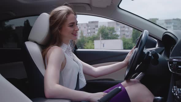 Young Attractive Girl in the Inside of the Car Looking at Camera and Smilling the Wind Waving Her