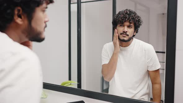 Young Indian Man Checks Skin and Teeth Looking in Mirror
