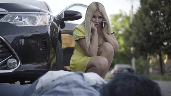 Portrait of Crying Beautiful Woman Sitting at Corpse of Lady Hit By Car, and Talking on the Phone