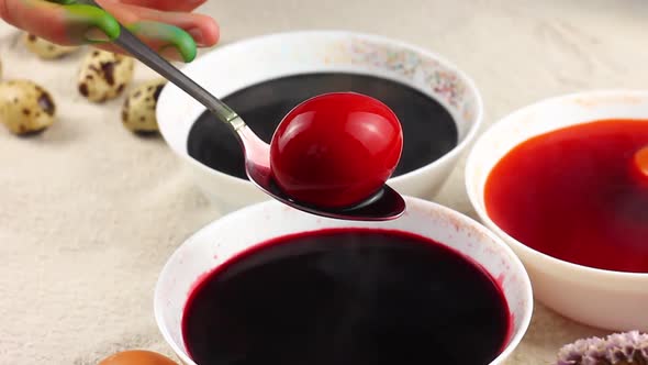Caucasian Child Paints an Easter Egg with a Metal Spoon and Dips It Into a White Bowl with Red Dye