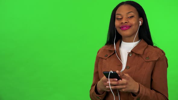 A Young Black Woman Listens To Music on a Smartphone - Green Screen Studio