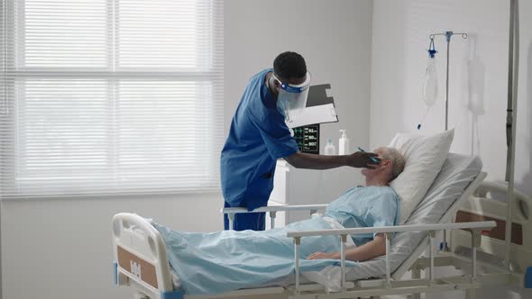 An Elderly Male Patient Lying in a Hospital Bed Connected to an ECG Machine Talks to a Black Doctor