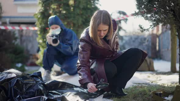 Portrait of Smart Concentrated Woman Examining Corpse with Magnifier As Colleague Taking Photos at