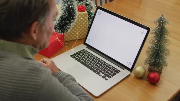 Caucasian senior man sitting at table making video call at home on laptop with copy space on screen