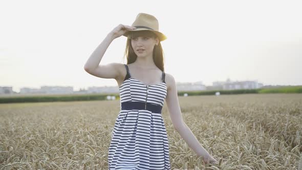 Cute Girl Puts on Hat and Walks Among Wheat Field with Smile