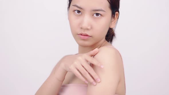 Slow motion of Asian girl with natural make up looking to camera and patting her body gently.