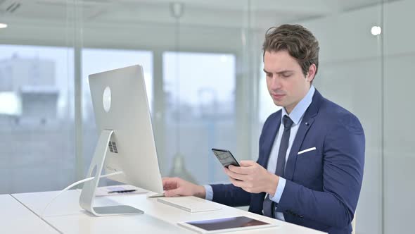 Young Businessman Talking on Smartphone and Working on Desk Top 