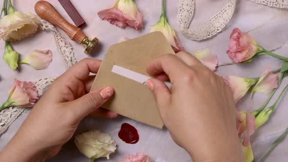 Hands opening and closing envelope with a MARRY ME card near pink flowers