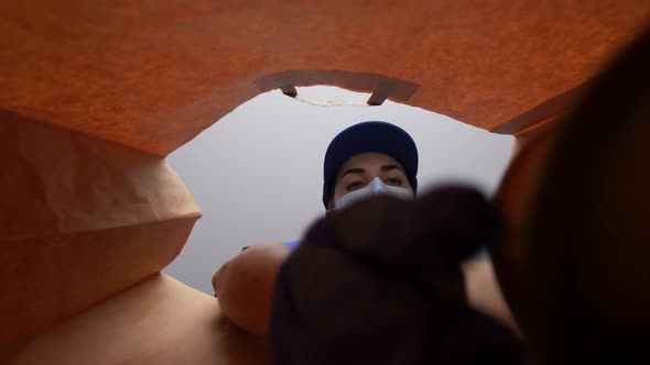 Woman in Gloves and Mask Packing Food in Paper Bag