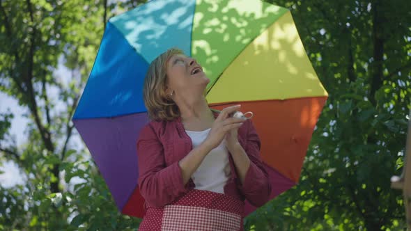 Portrait of Charming Caucasian Senior Woman Spinning Colorful Umbrella in Slow Motion Looking Up