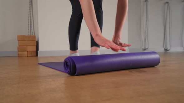 Woman rolling up yoga mat after training in studio. Girl folding fitness mat on floor at yoga studio