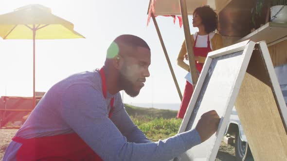 African american man wearing apron writing on food menu slate board of the food truck