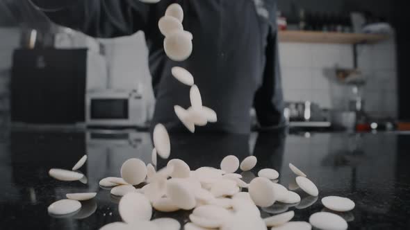 Chef Chocolatier Pours Milk Chocolate Drops To the Marble Table in Slow Motion, Raw Materials for