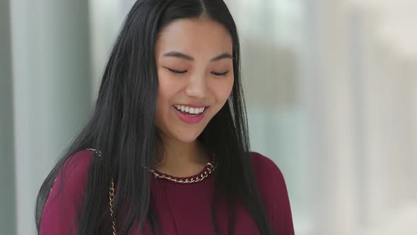 Close up of Asian woman looking at her phone and then smiling and laughing then looking back down