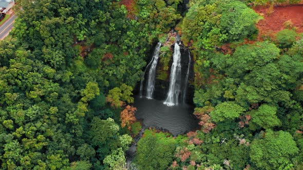 Drone moves away from a mountain waterfall in the forest, Opaekaa Falls, Kauai, Hawaii, USA