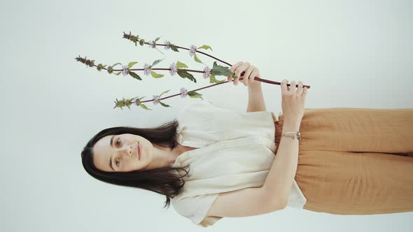 Happy Woman Holding Flower Twig and Posing for Camera in Studio