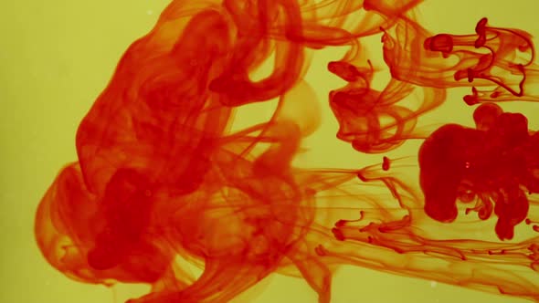 Red Ink Drips and Swirls in Clear Water Over Mustard Yellow Background in Slowmotion