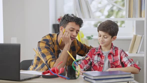 Focused Middle Eastern Teenager Talking with Little Concentrated Brother Doing Homework Indoors