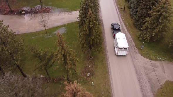 Black pick up truck towing horse trailer through small town, aerial follow view