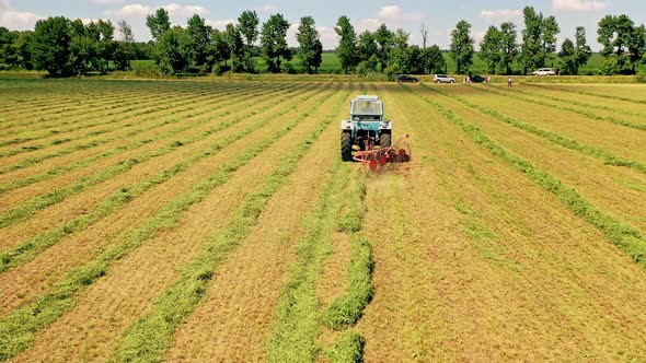 Agricultural process with green grass in the field. Tractor is working in summer on the grassland