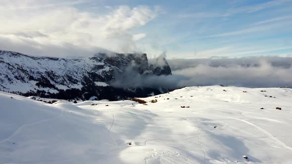 Drone footage from the Italian Dolomites on a sunny winter day, while clouds move in front of the pe