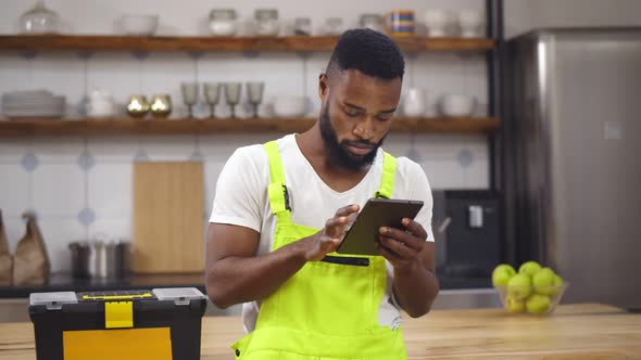 African Handyman Using Digital Tablet Standing in Home Kitchen