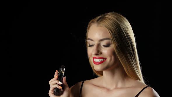 Girl Smiles, Inhales and Exhales the Smoke of an Electronic Cigarette. Black Background