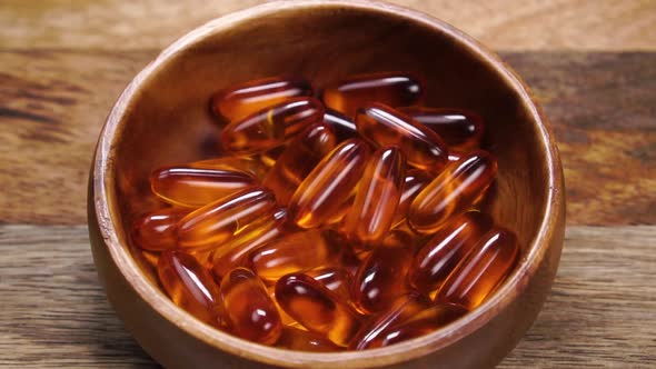 Omega 3 capsules fall into a wooden bowl on a rustic wood surface in slow motion