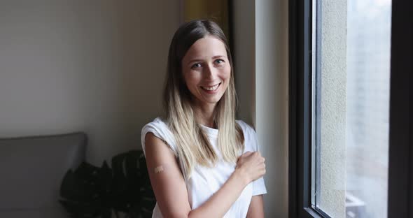 Happy Young Caucasian Woman with Blonde Hair Showing COVID19 Vaccine Bandage on Arm When Standing at