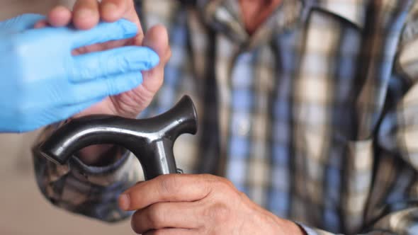 Close-up of a doctor's hands give support and care to a senior citizen patient with a walking stick.